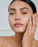 Nuria Hydrate Moisture Replenishing Serum - woman holding bottle while massaging serum into cheek with fingers