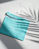 Nuria Hydrate Nourishing Under-Eye Masks - open envelope and pair of under-eye masks on countertop with frond shadows over top