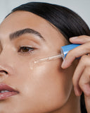 Nuria Defend Skin Restoring Serum - woman using dropper to apply serum to cheek
