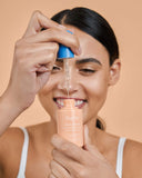 Nuria Defend Skin Restoring Serum - woman smiling while holding dropper above bottle showing serum