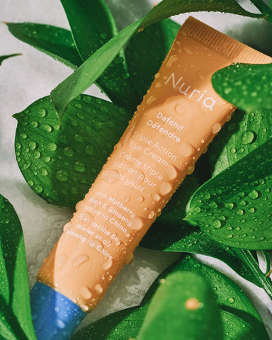 Nuria Defend Triple Action Eye Cream - tube with droplets laying among green leaves
