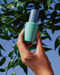 Nuria Hydrate Moisture Replenishing Serum - bottle held up against tree and sky background