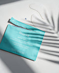 Nuria Hydrate Nourishing Under-Eye Masks - open envelope and pair of under-eye masks on countertop with frond shadows over top