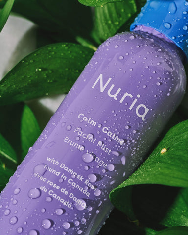 Nuria Calm Facial Mist -- bottle with water droplets laying in green leaves