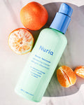 Nuria Rescue Rebalancing Cleanser - bottle on marble counter with ingredient, mandarin oranges, surrounding