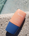 Nuria Defend Matte Finish Daily Moisturizer Mineral Sunscreen SPF 30 - bottle resting on stone with water on background