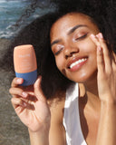 Nuria Defend Matte Finish Daily Moisturizer Mineral Sunscreen SPF 30 - woman at beach smiling and applying sunscreen to cheek